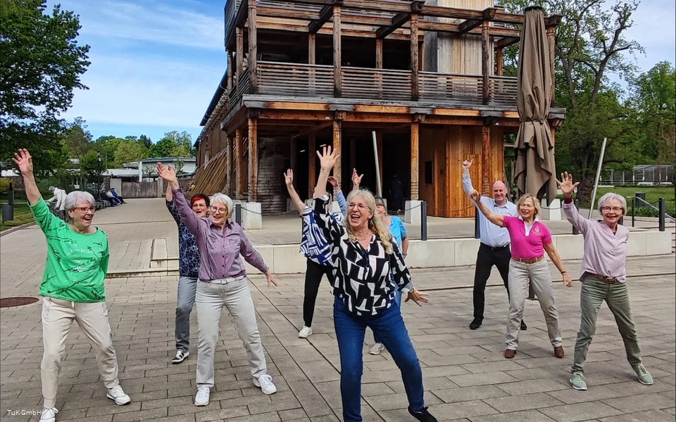 Eine Gruppe unterschiedlicher Menschen tanzt im Kurpark Bad Sassendorf. Alle haben Spaß dabei und lachen.